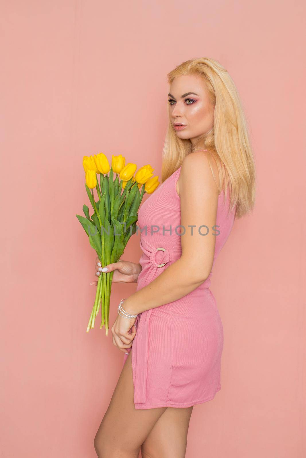 Blonde in pink summer dress holding bouquet of yellow tulips by Bonda