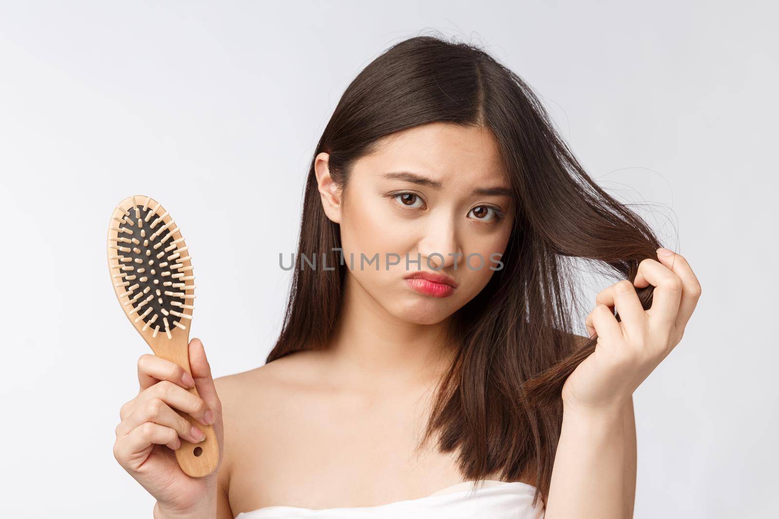 Upset stressed young Asian woman holding damaged dry hair on hands over white isolated background