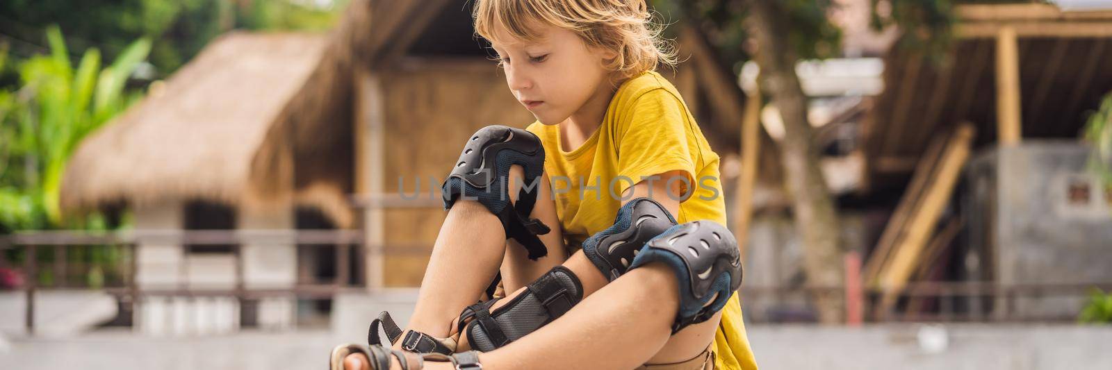 Boy puts on knee pads and armbands before training skate board BANNER, LONG FORMAT by galitskaya