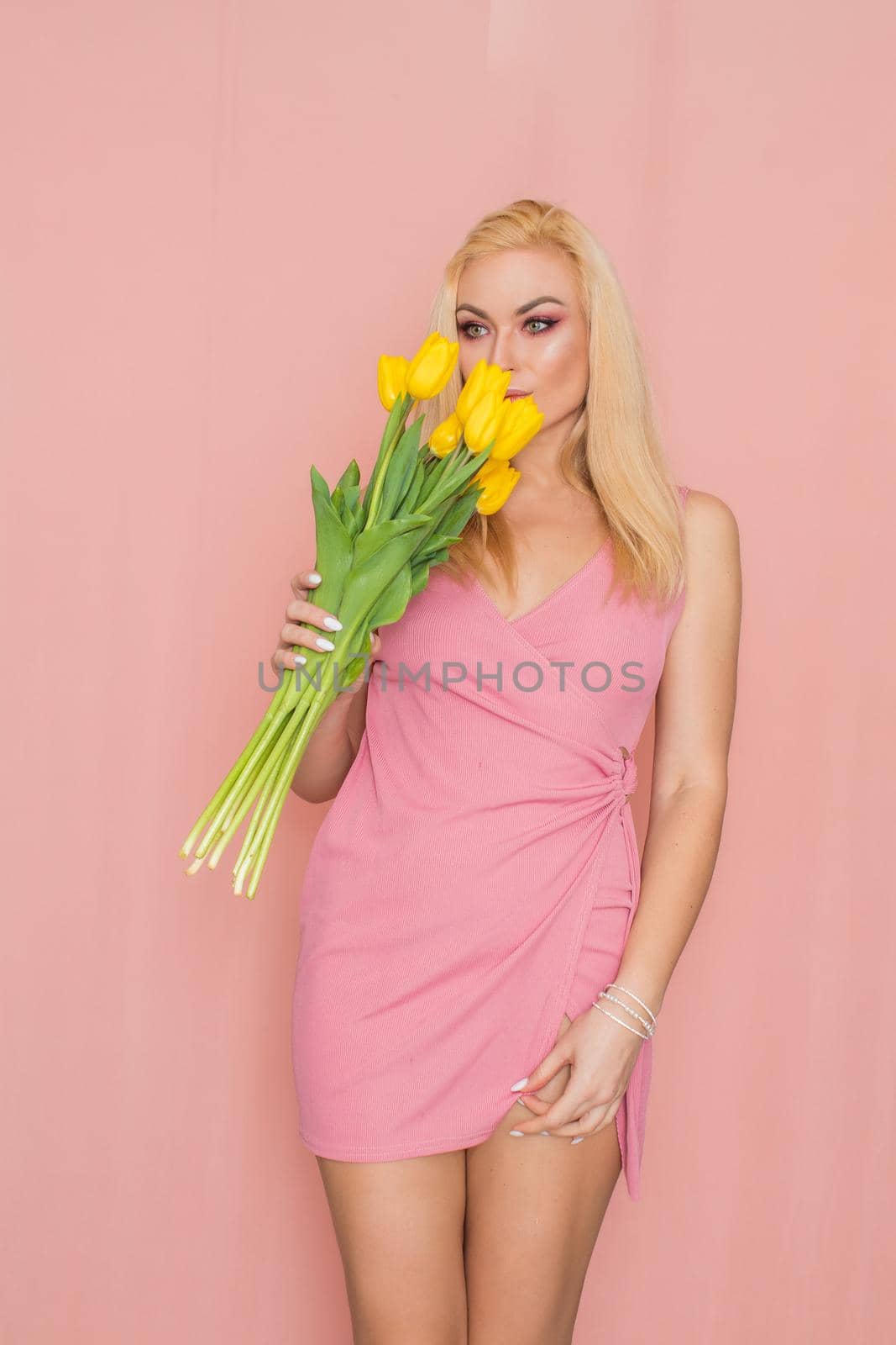 Blonde in pink summer dress holding bouquet of yellow tulips by Bonda