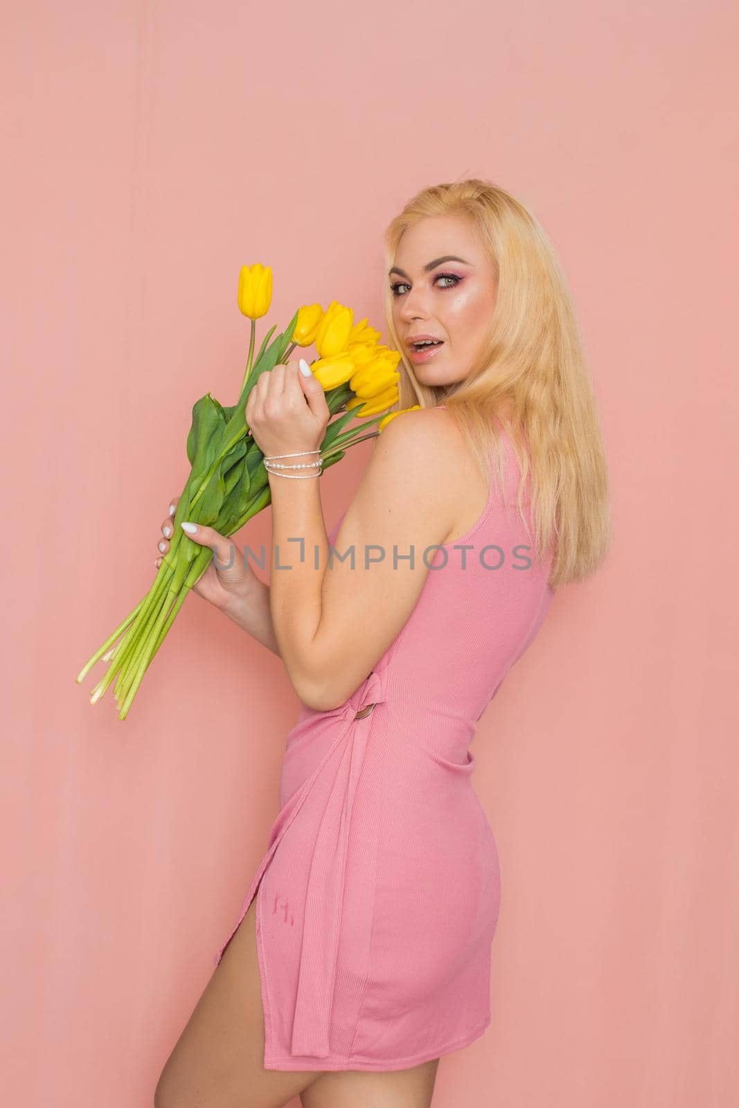 Blonde in pink summer dress holding bouquet of yellow tulips by Bonda