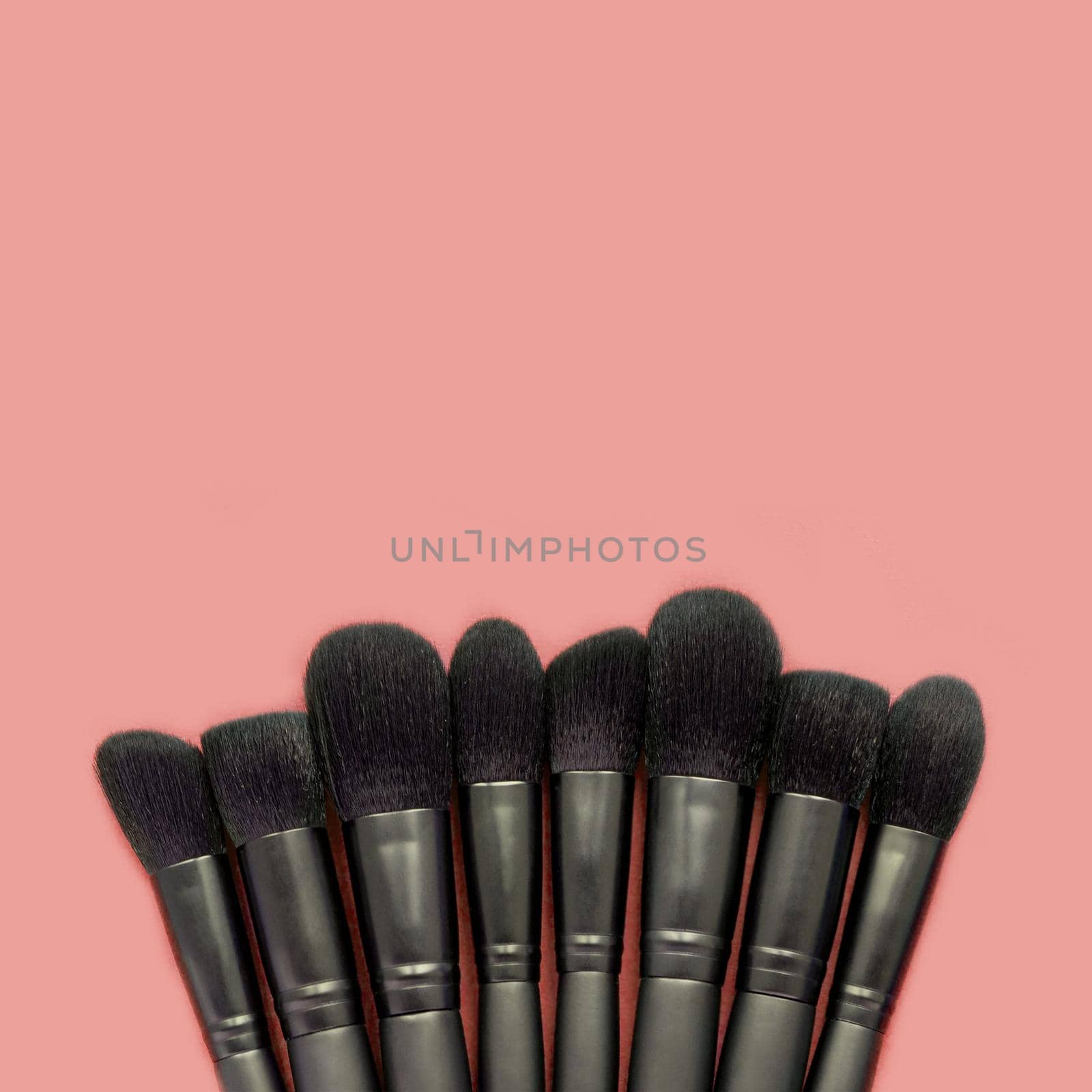 Flat lay of black makeup brushes on pastel peach color background
