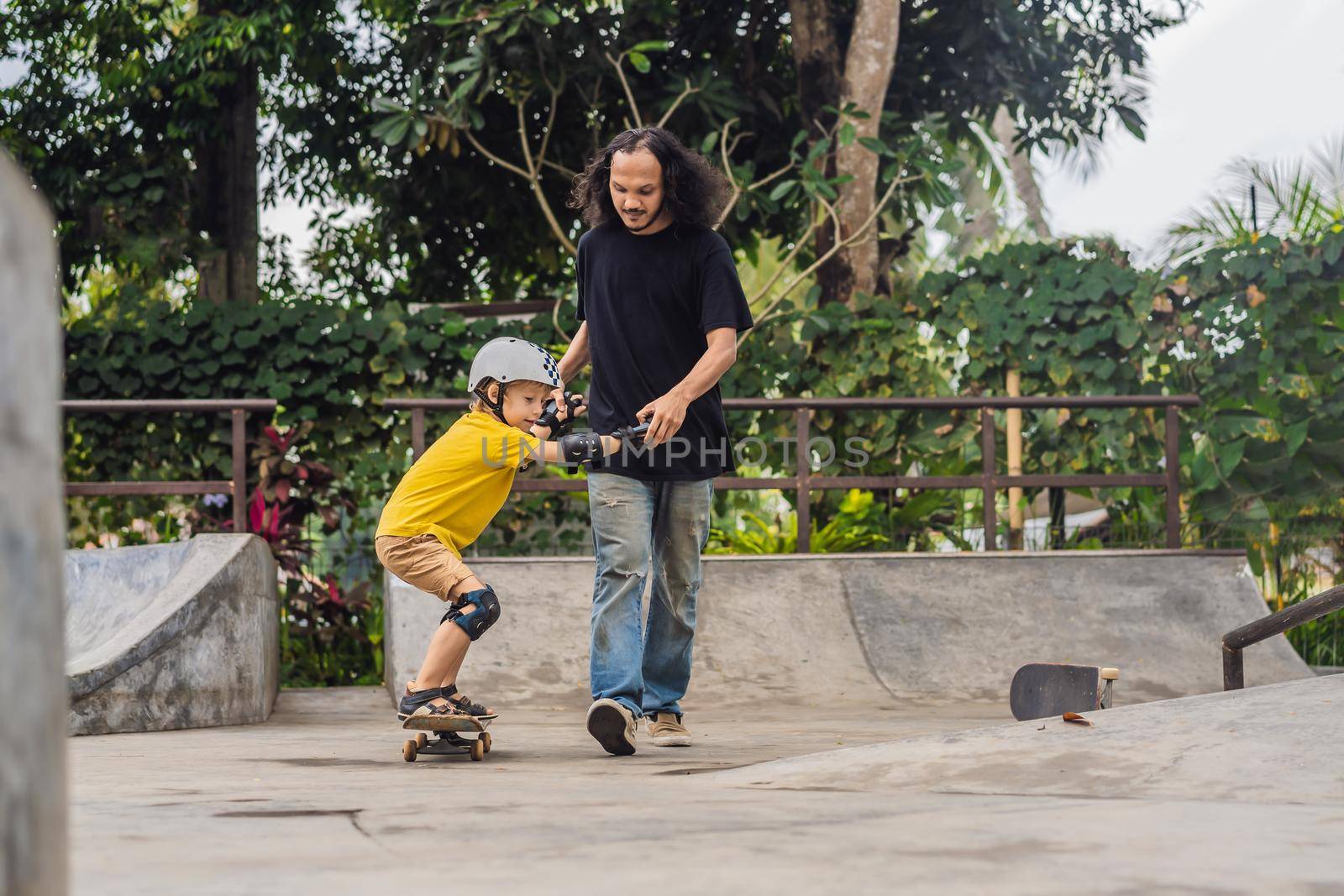 Athletic boy learns to skateboard with asian trainer in a skate park. Children education, sports. Race diversity.