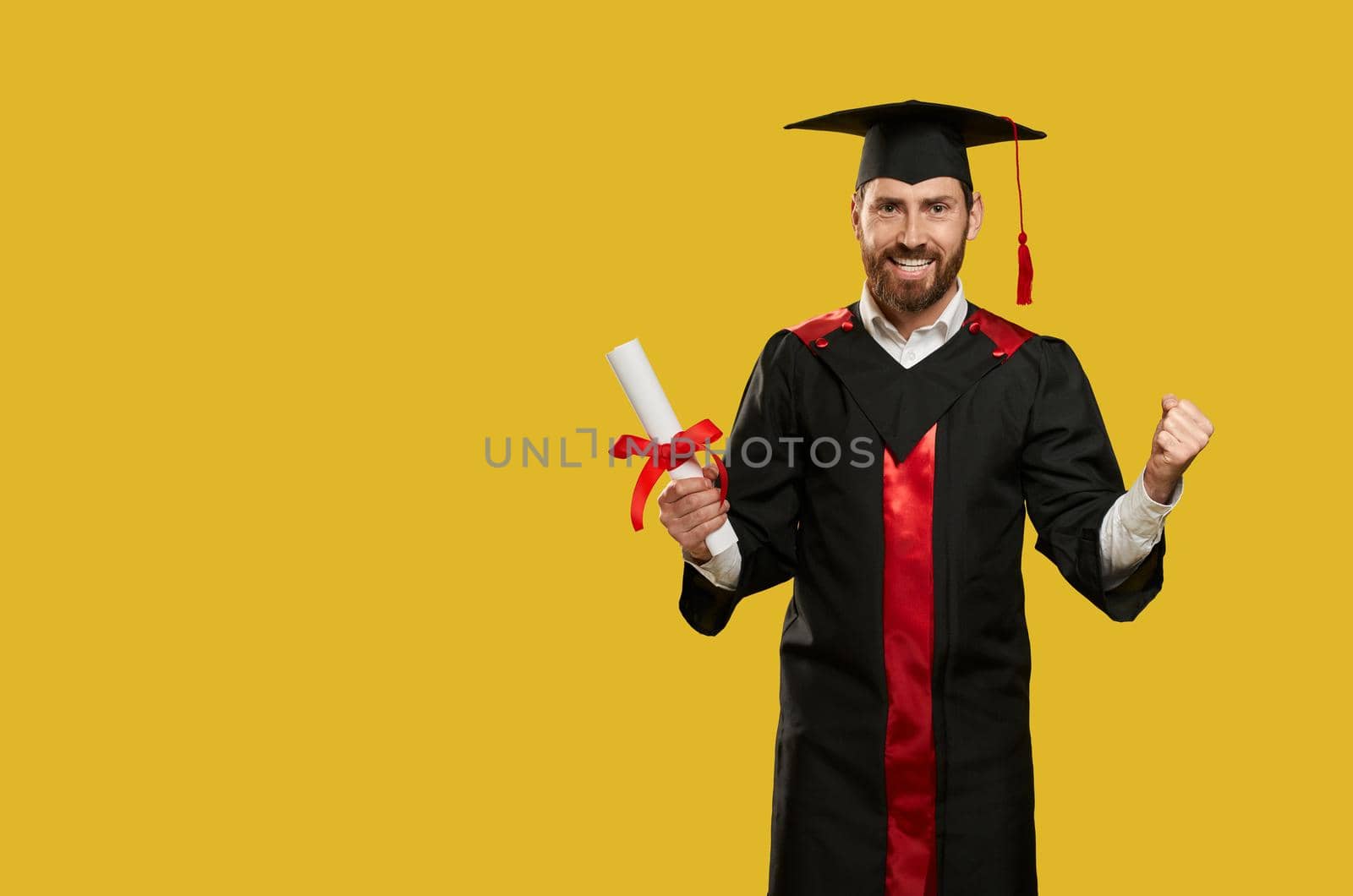 Front view of cheerful boy graduating from college, university. Male with bachelor, master degree standing, holding diploma, looking at camera, smiling. Concept of youth.