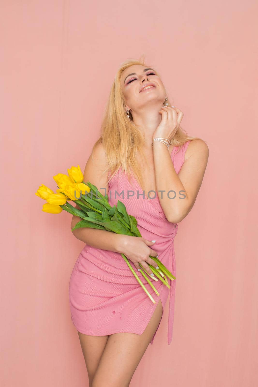 Blonde in pink summer dress holding bouquet of yellow tulips by Bonda