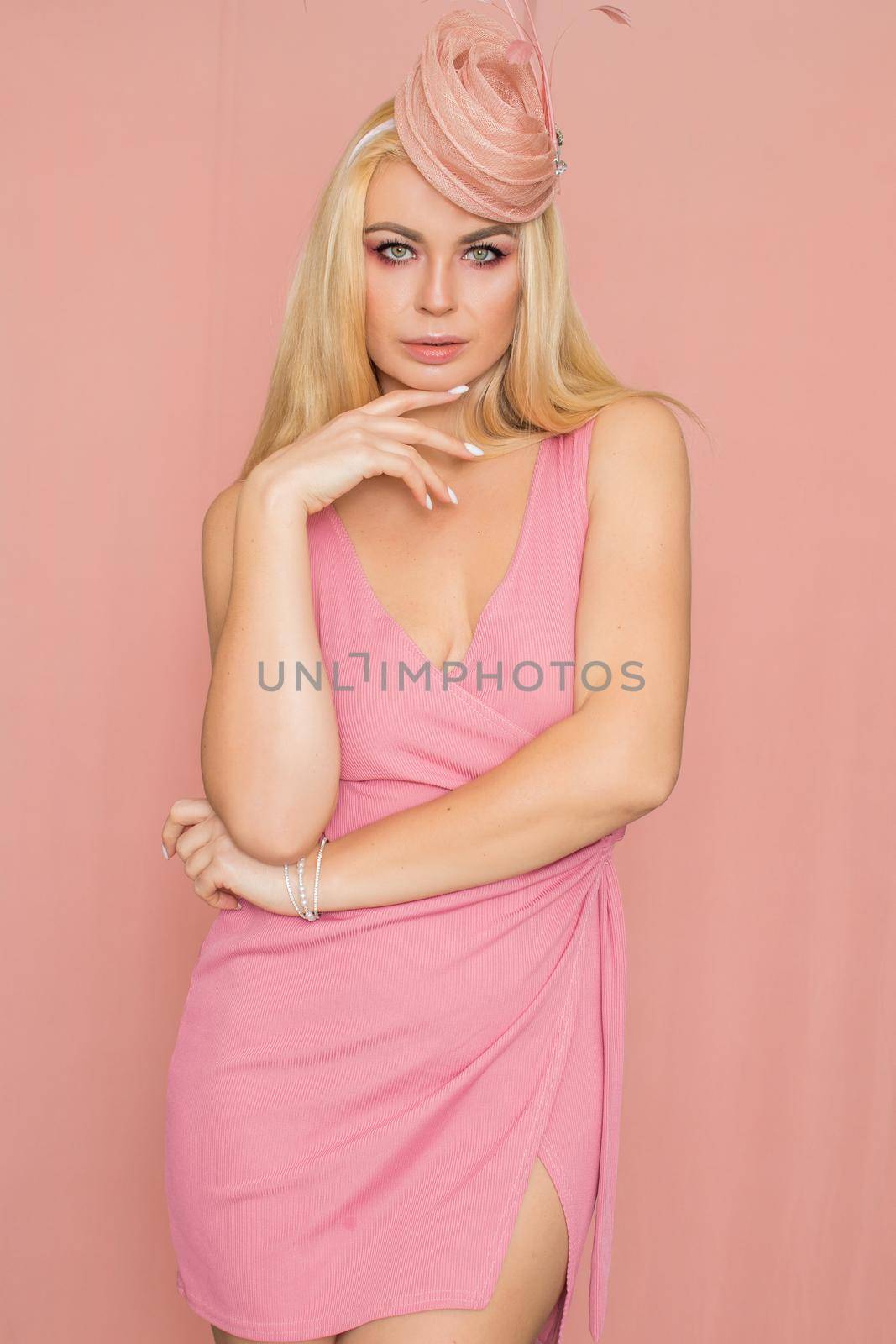 Adult blonde woman in pink dress posing over rosy background. Spring-summer clothing. Wearing hat
