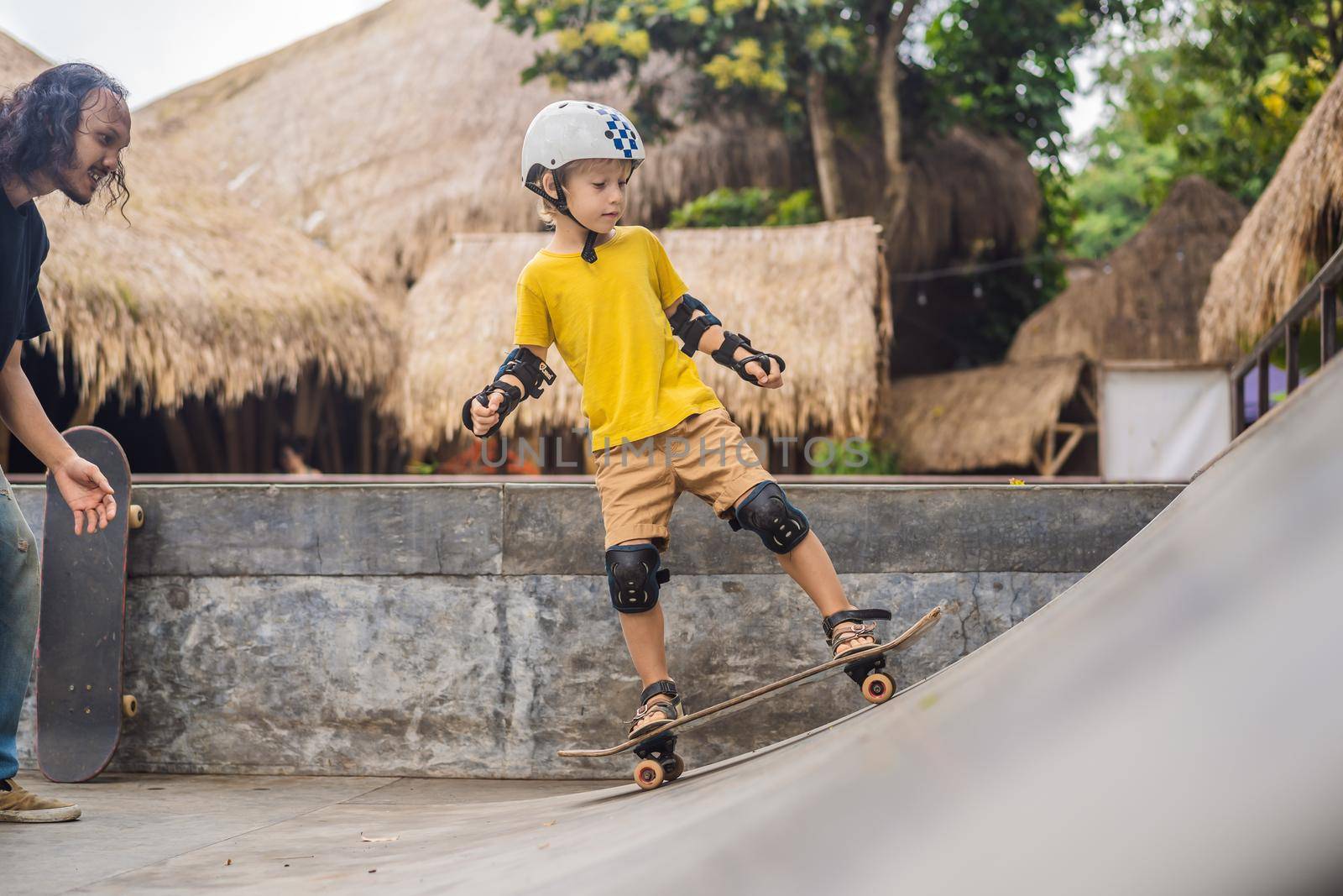 Athletic boy learns to skateboard with asian trainer in a skate park. Children education, sports. Race diversity.