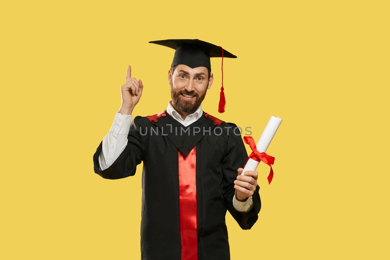 Front view of happy young man graduating from university, college. Boy with beard standing, smiling, raising finger, holding diploma, surprised. Concept of youth and knowledge.