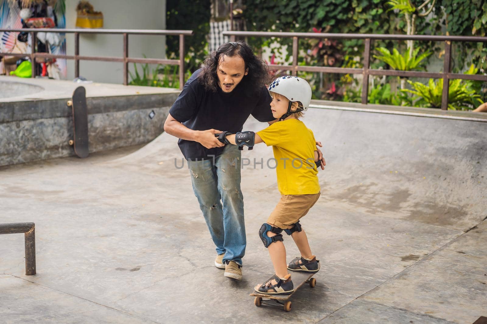 Athletic boy learns to skateboard with asian trainer in a skate park. Children education, sports. Race diversity.