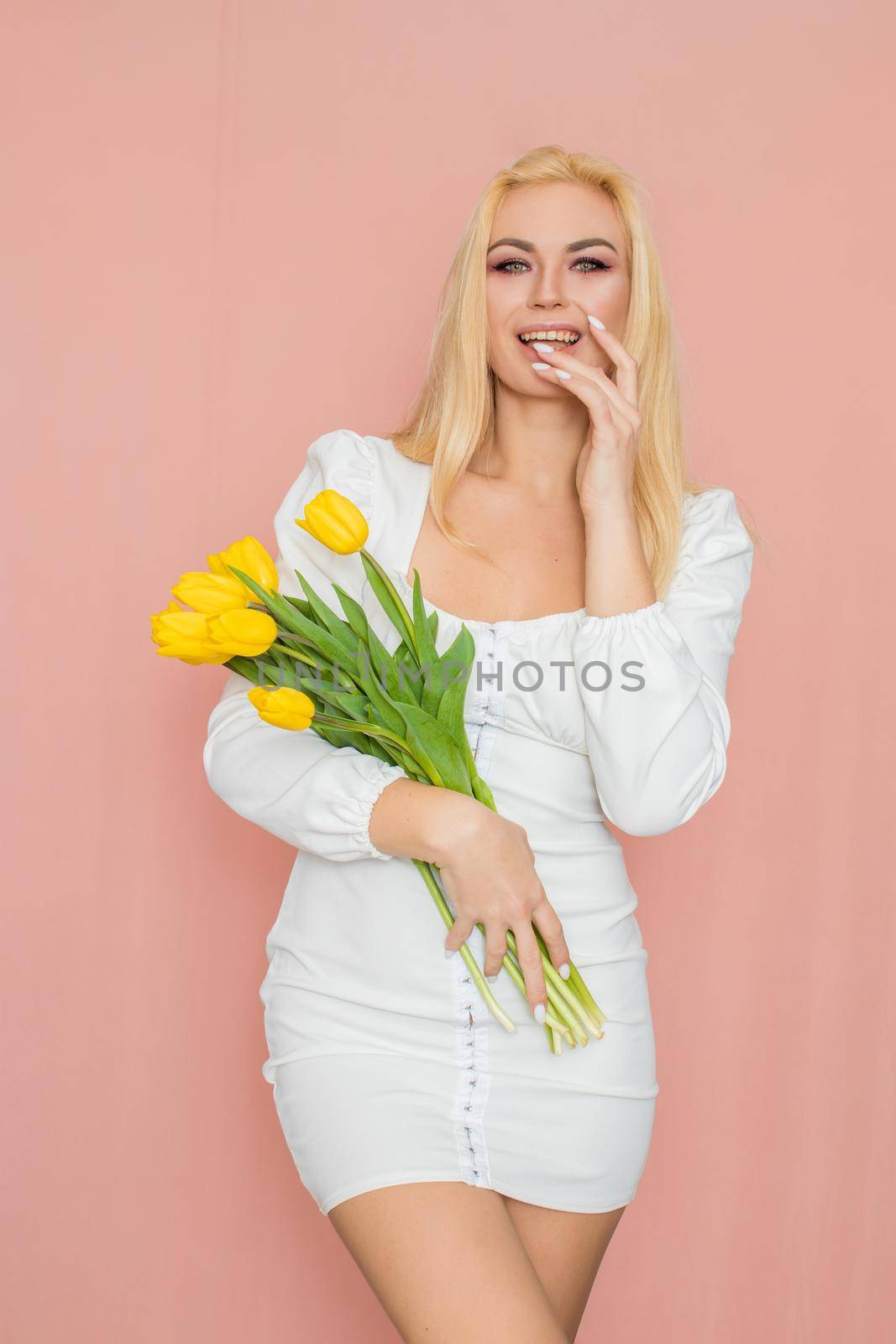 Blonde woman in spring white dress holding bouquet in her hands by Bonda