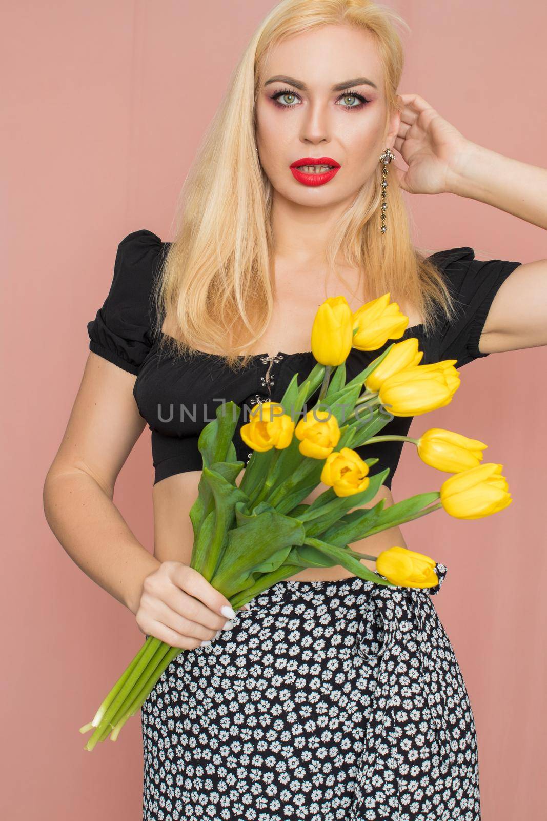 Summer fashion portrait blonde woman. Sexy look in black top and skirt. Red lips. Holding yellow tulips in her hands