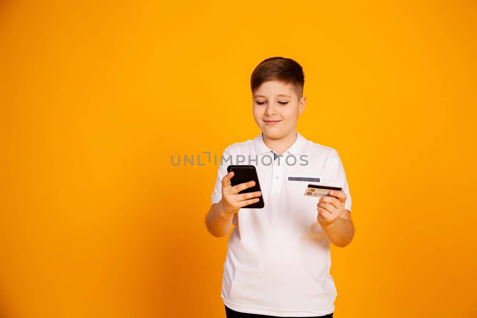 The boy holds a credit card and the smartphone makes purchases. Happy young man uses a smartphone and a bank card to shop online. Handsome smiling guy holds a bank card and mobile phone