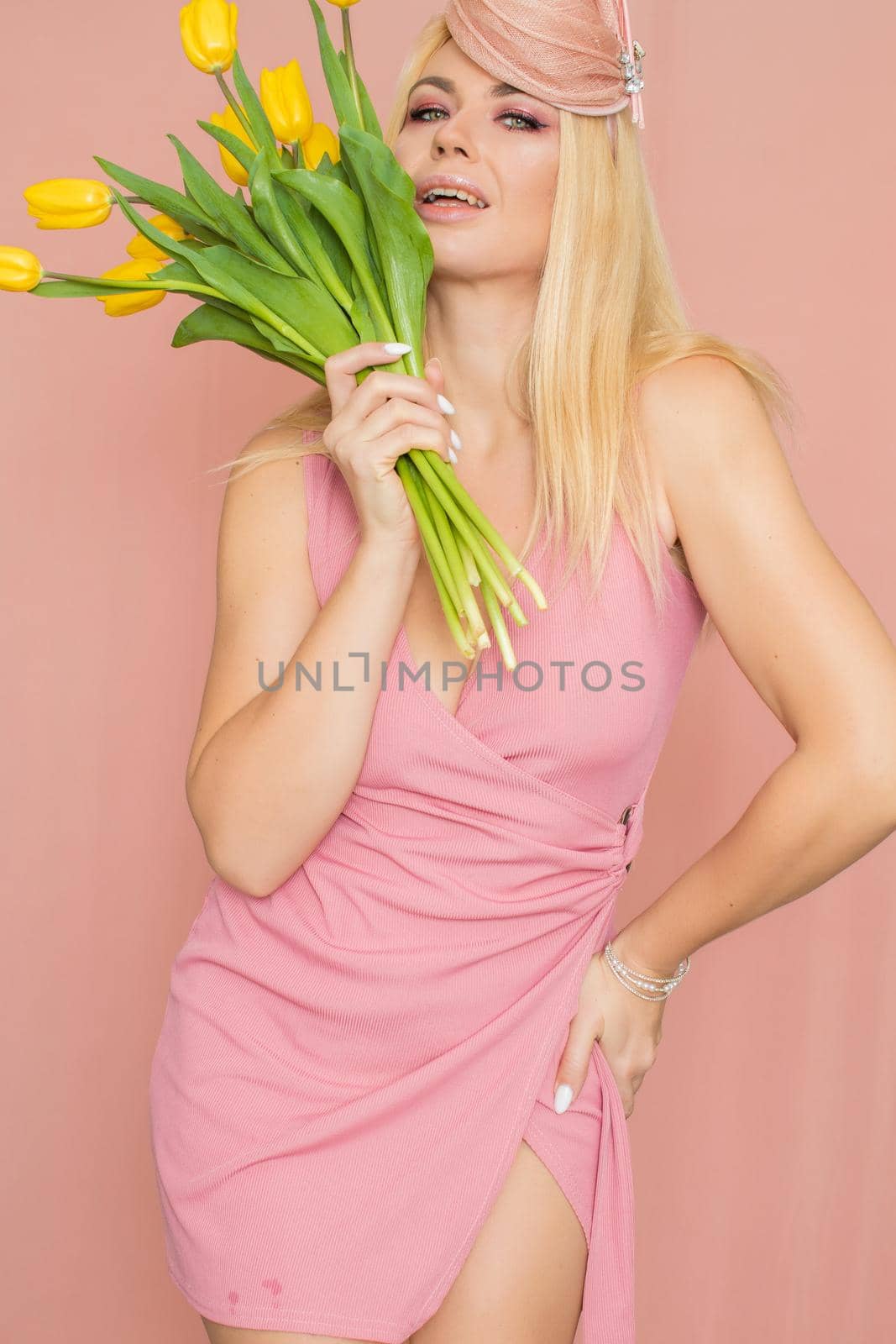 Blonde woman in pink hat holsing yellow tulips by Bonda
