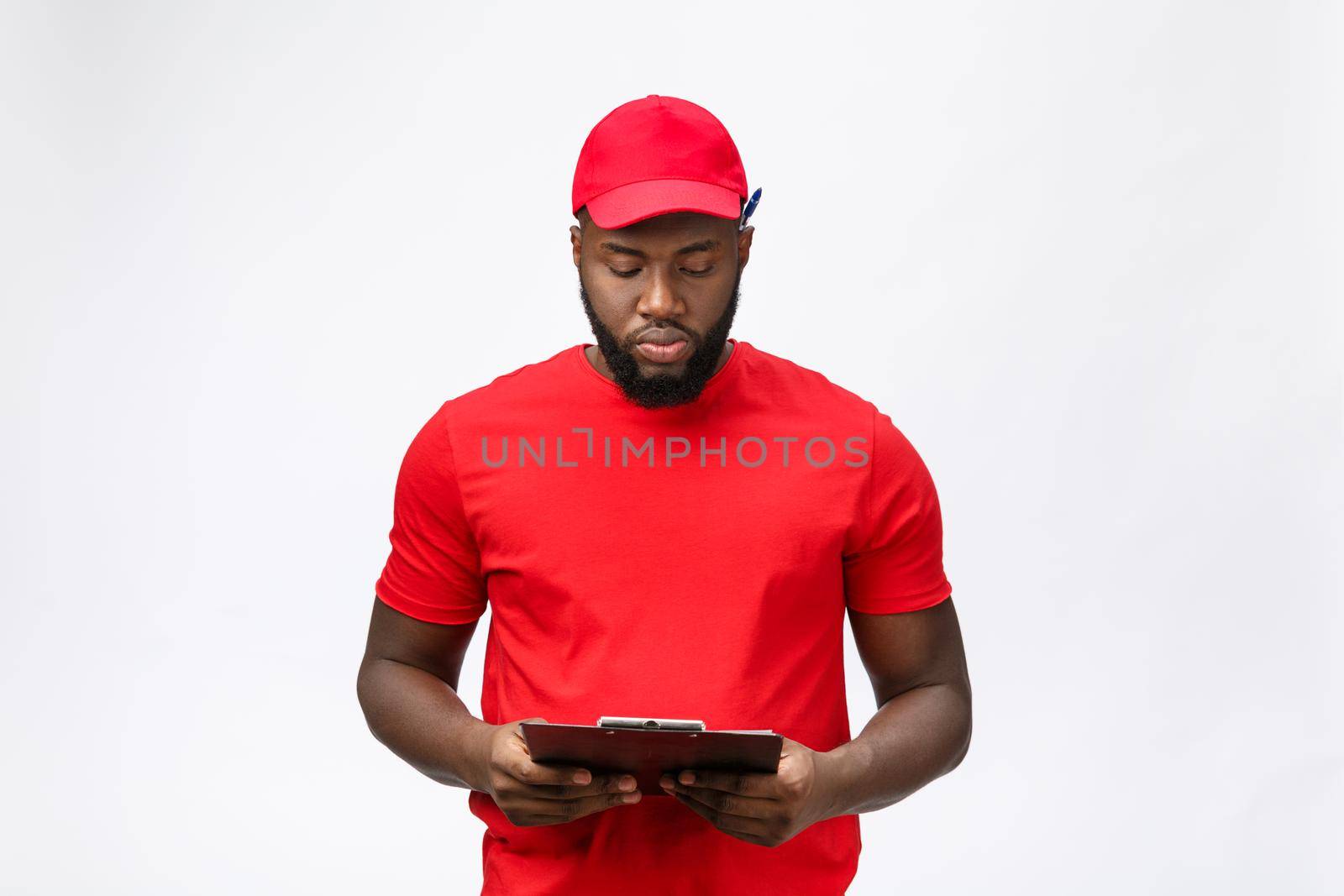 Thoughtful african american young delivery man writing on clipboard.