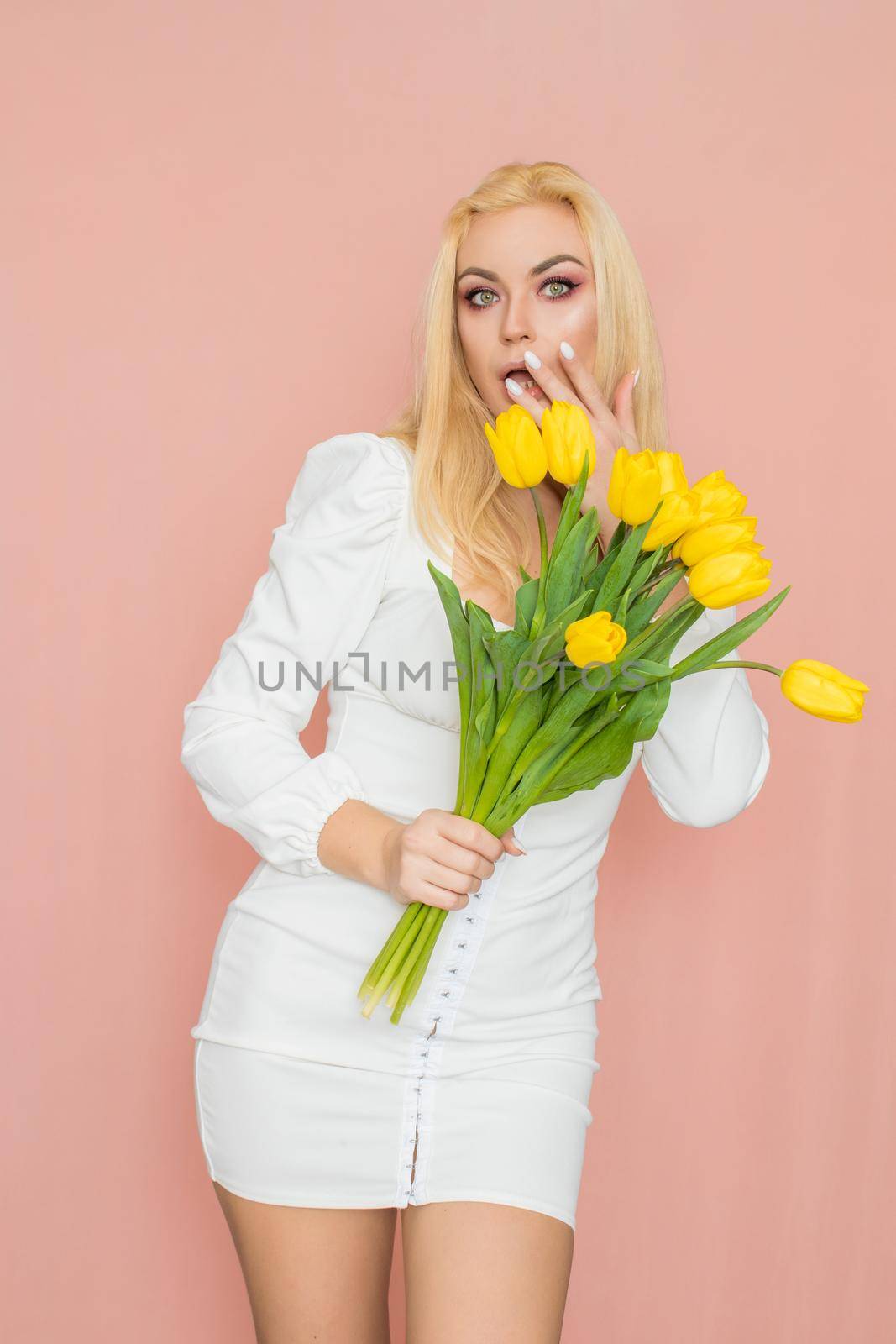 Blonde woman in spring white dress holding bouquet in her hands by Bonda