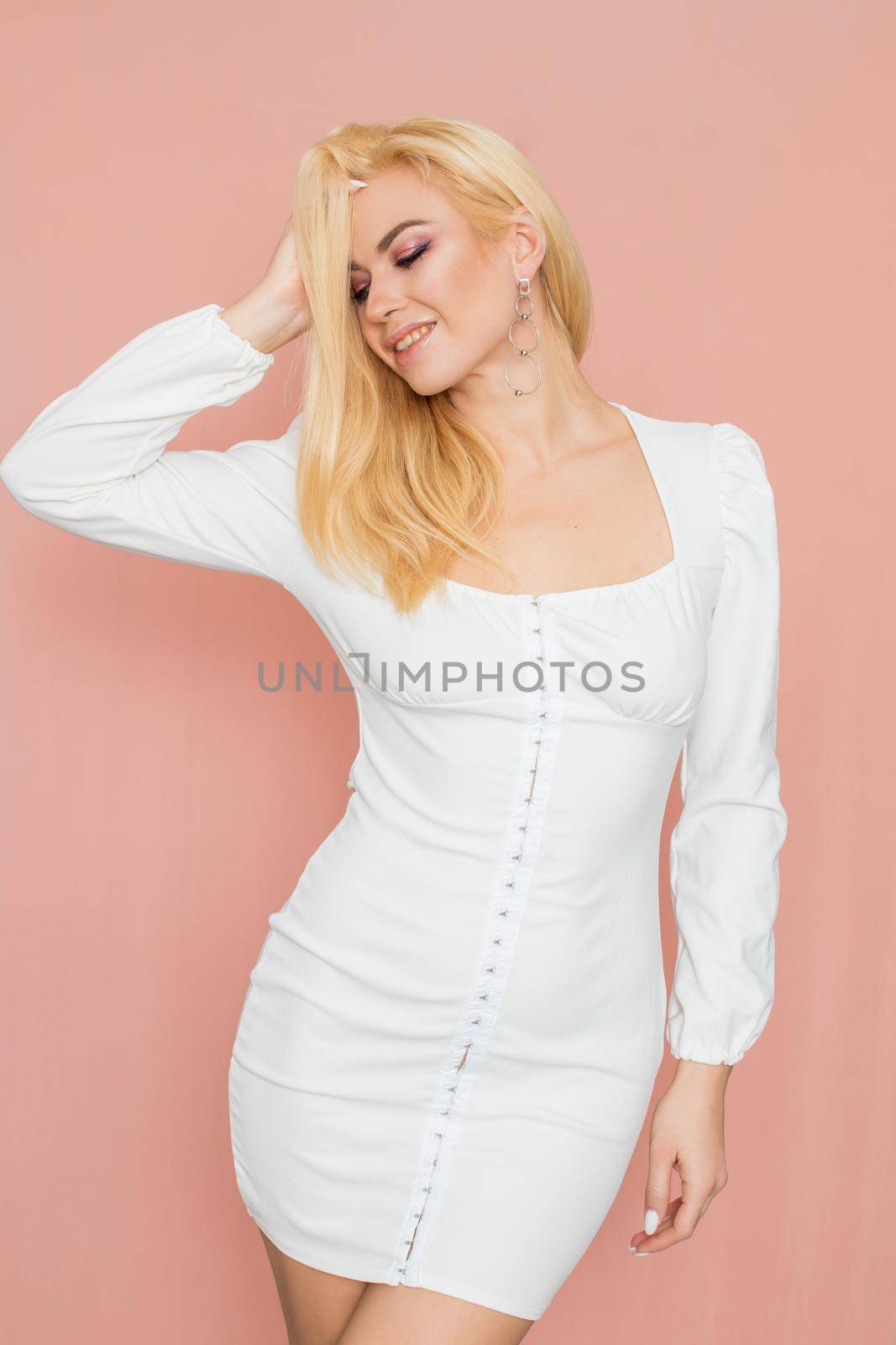 Spring fashion photo of blonde woman posing over pink background. Wearing white vintage dress with long sleeves