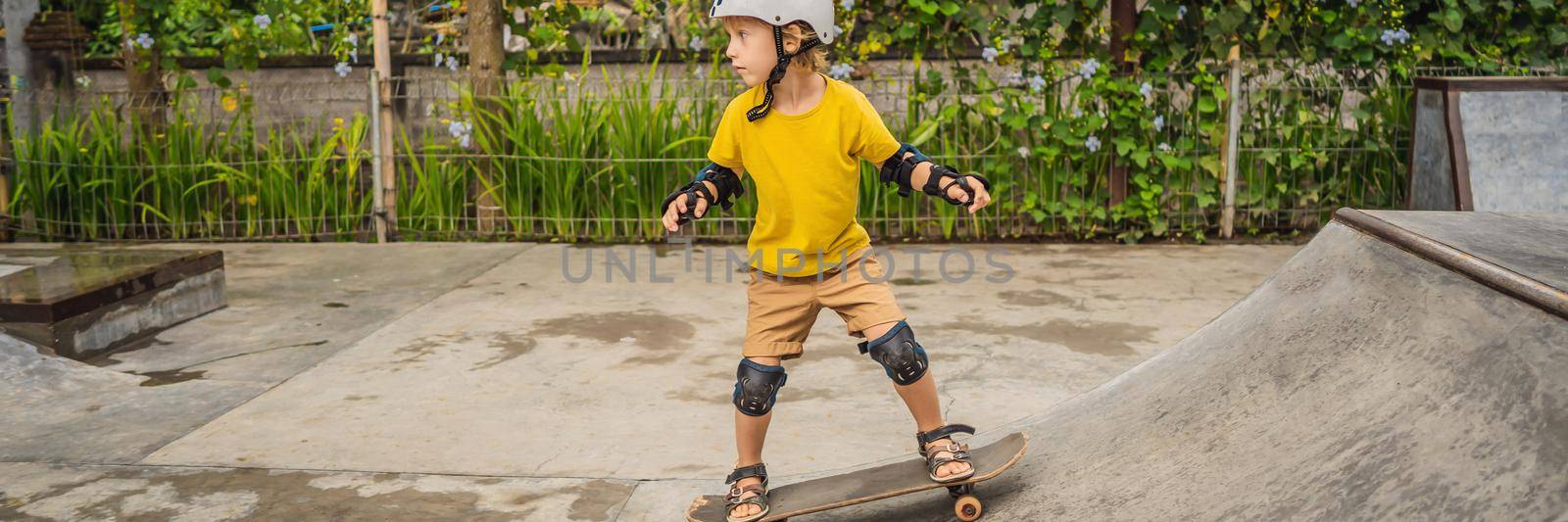 Athletic boy in helmet and knee pads learns to skateboard with in a skate park. Children education, sports BANNER, LONG FORMAT by galitskaya