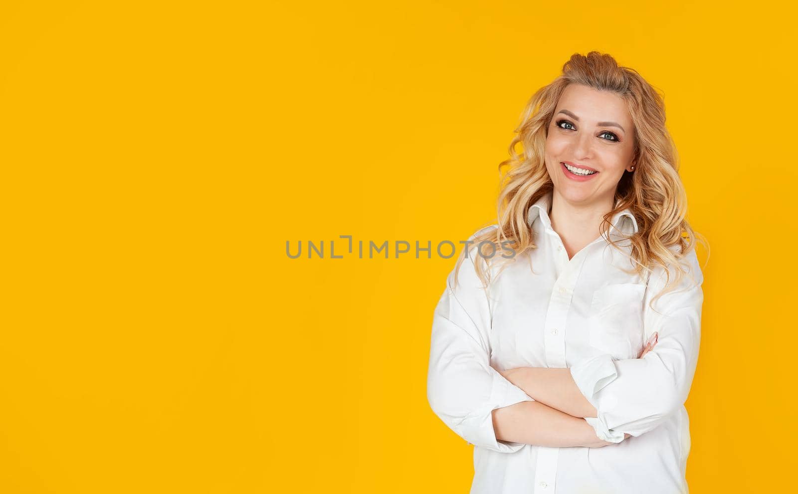 Portrait of a joyful and cheerful cute Caucasian woman in a white shirt who jokes cheerfully, entertains the conversation, smiles and laughs at the camera, on a yellow background