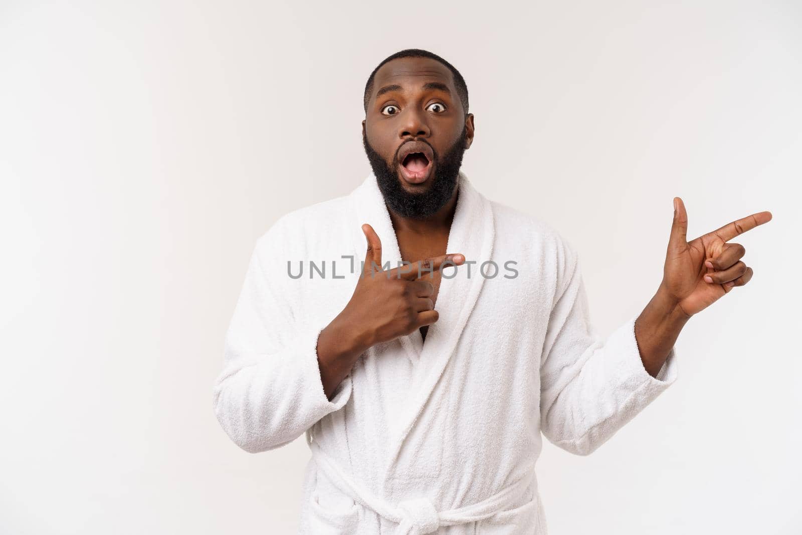 Black guy wearing a bathrobe pointing finger with surprise and happy emotion. Isolated over whtie background