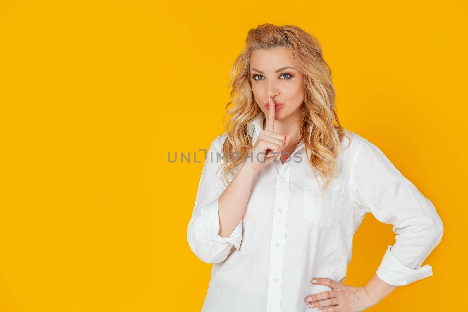 A serious woman silently looks at the camera, pressing her index finger to her lips, frowning disapprovingly, scolding for being too loud. says: shut up, shut up, shh quietly, please.