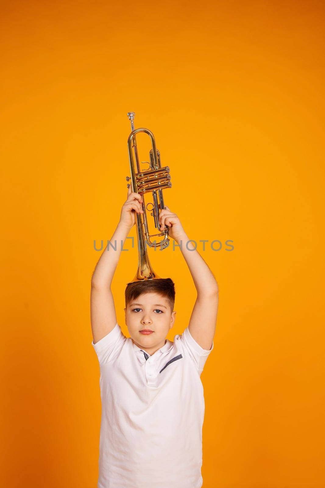 A boy in a white T-shirt holds a trumpet with a musical instrument on his head.
