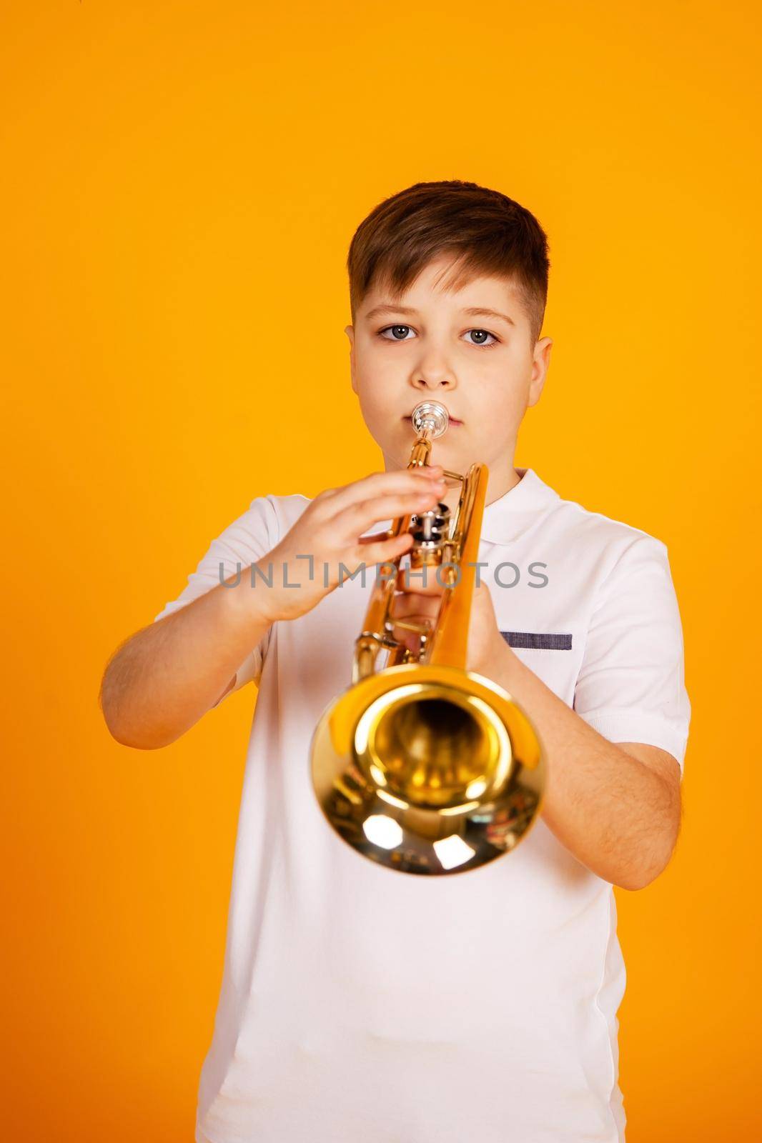 A boy plays the trumpet. A handsome teenager boy in a white T-shirt plays trumpet musical instrument