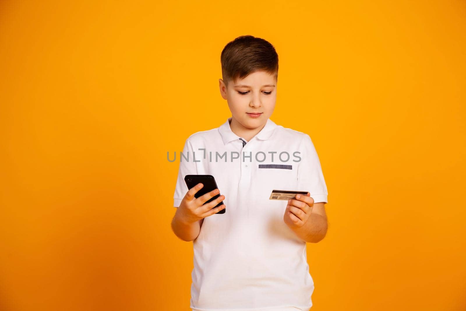 The boy pays with a credit card. Smiling teenage boy holding a credit card and smartphone, buying through the Internet
