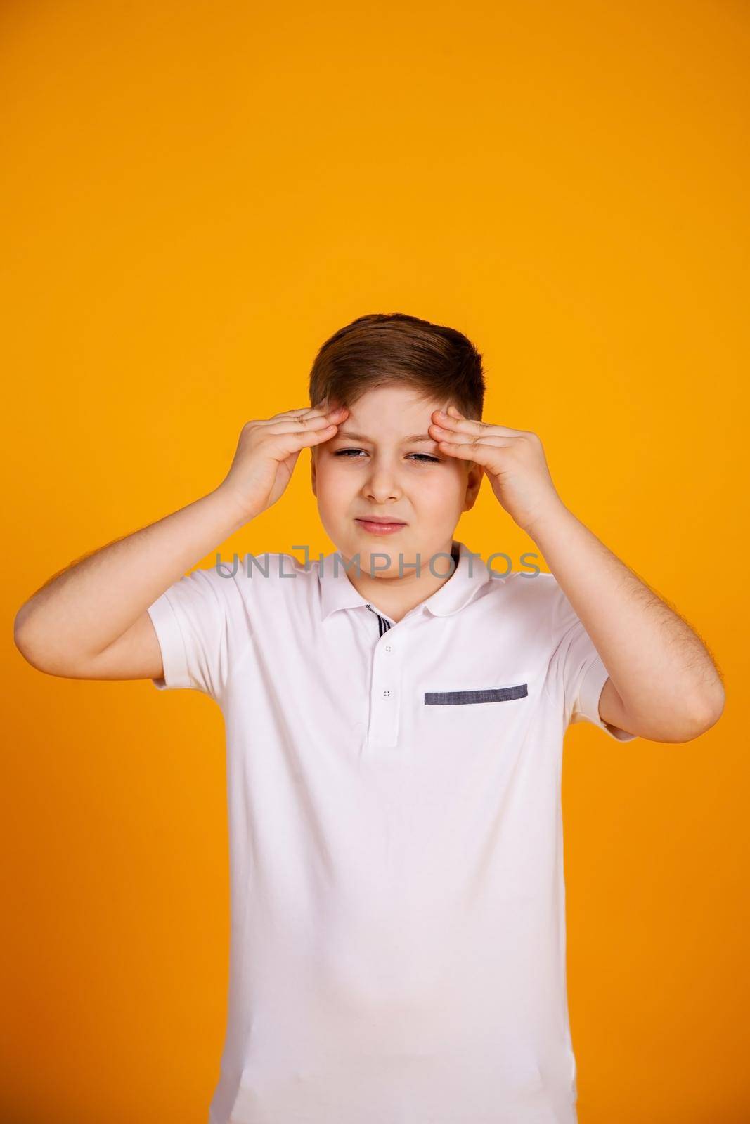 A boy with a headache. Caucasian child on a yellow background suffering from headache and migraine. Hands on the head.