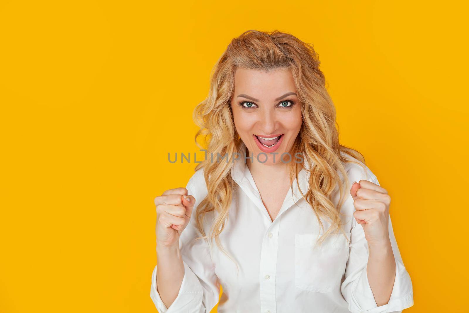 Cheerful, happy woman raising her hands with her fist, cheering for the team, winning a huge bet, playing in the casino in delight, cheering friends, watching football, yellow background