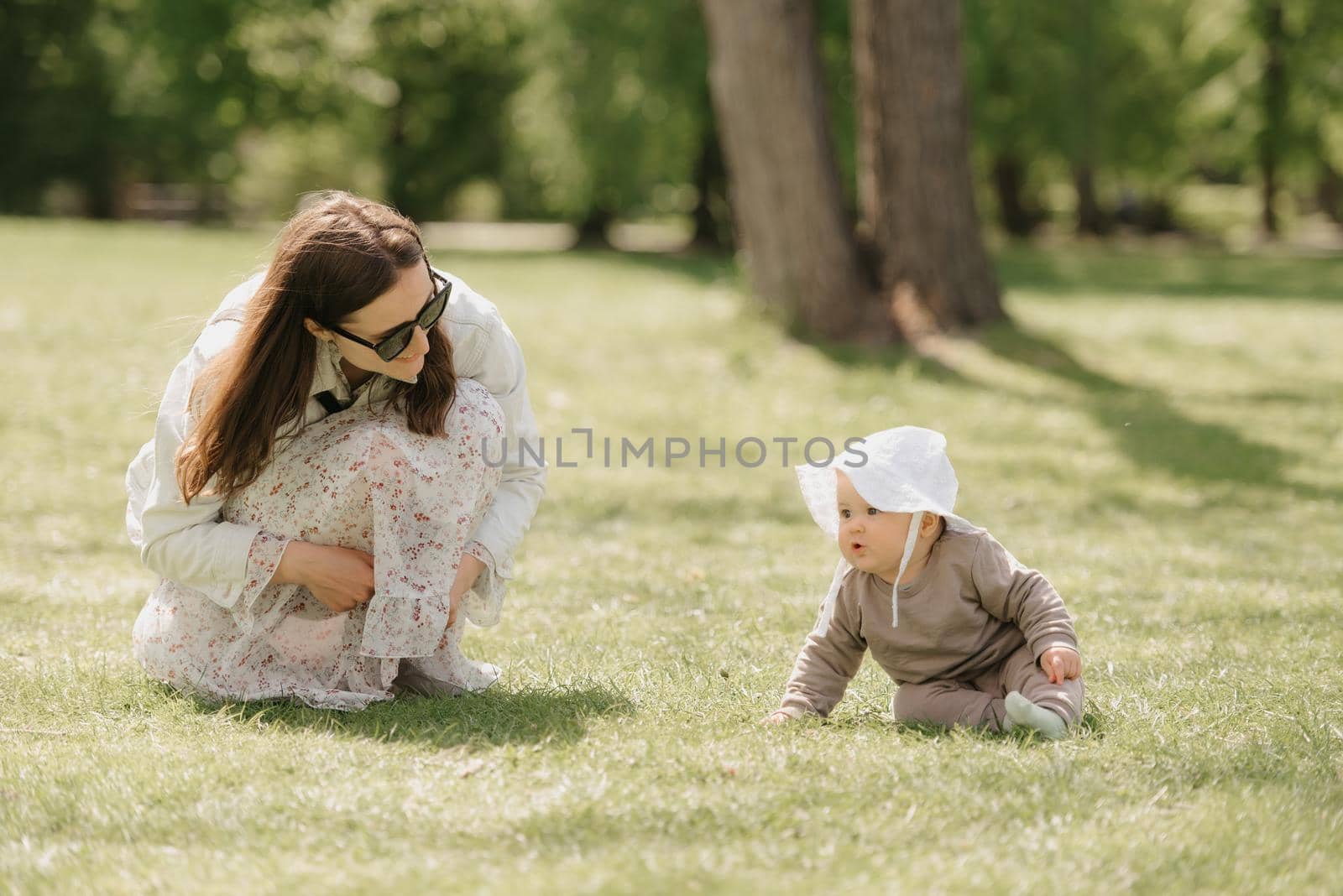 A young mother is playing with her 7-month daughter in the meadow. An infant girl is crawling on the grass.