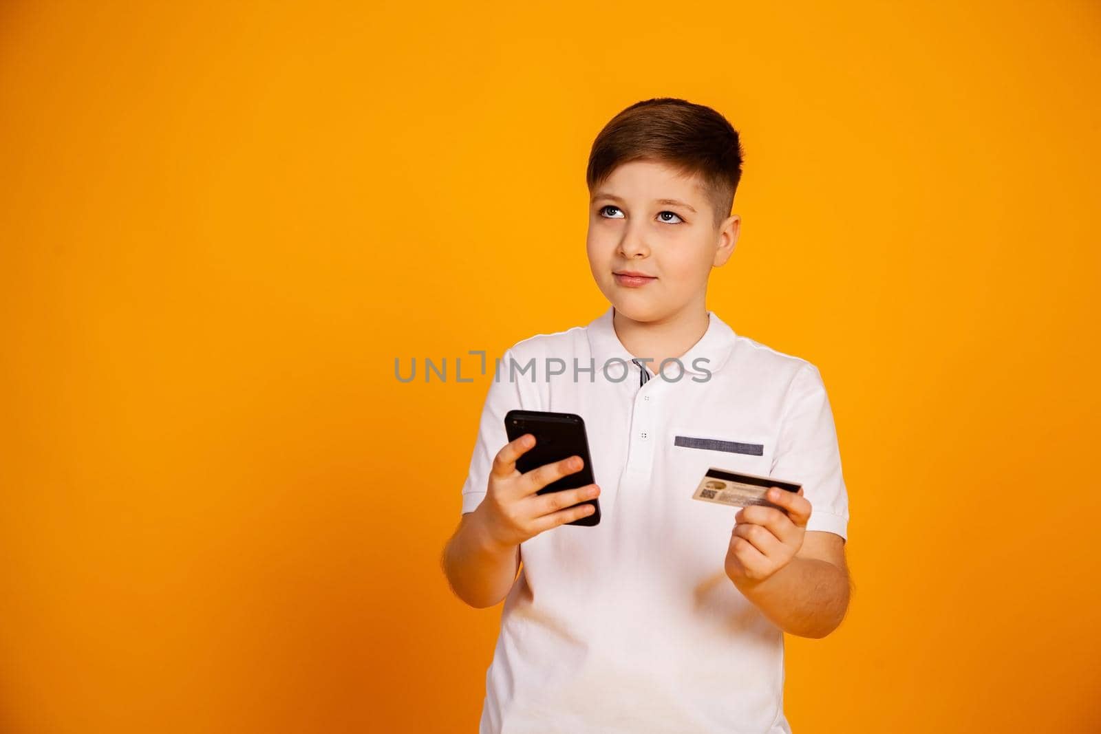The boy holds a credit card and the smartphone makes purchases. Happy young man uses a smartphone and a bank card to shop online. Handsome smiling guy holds a bank card and mobile phone