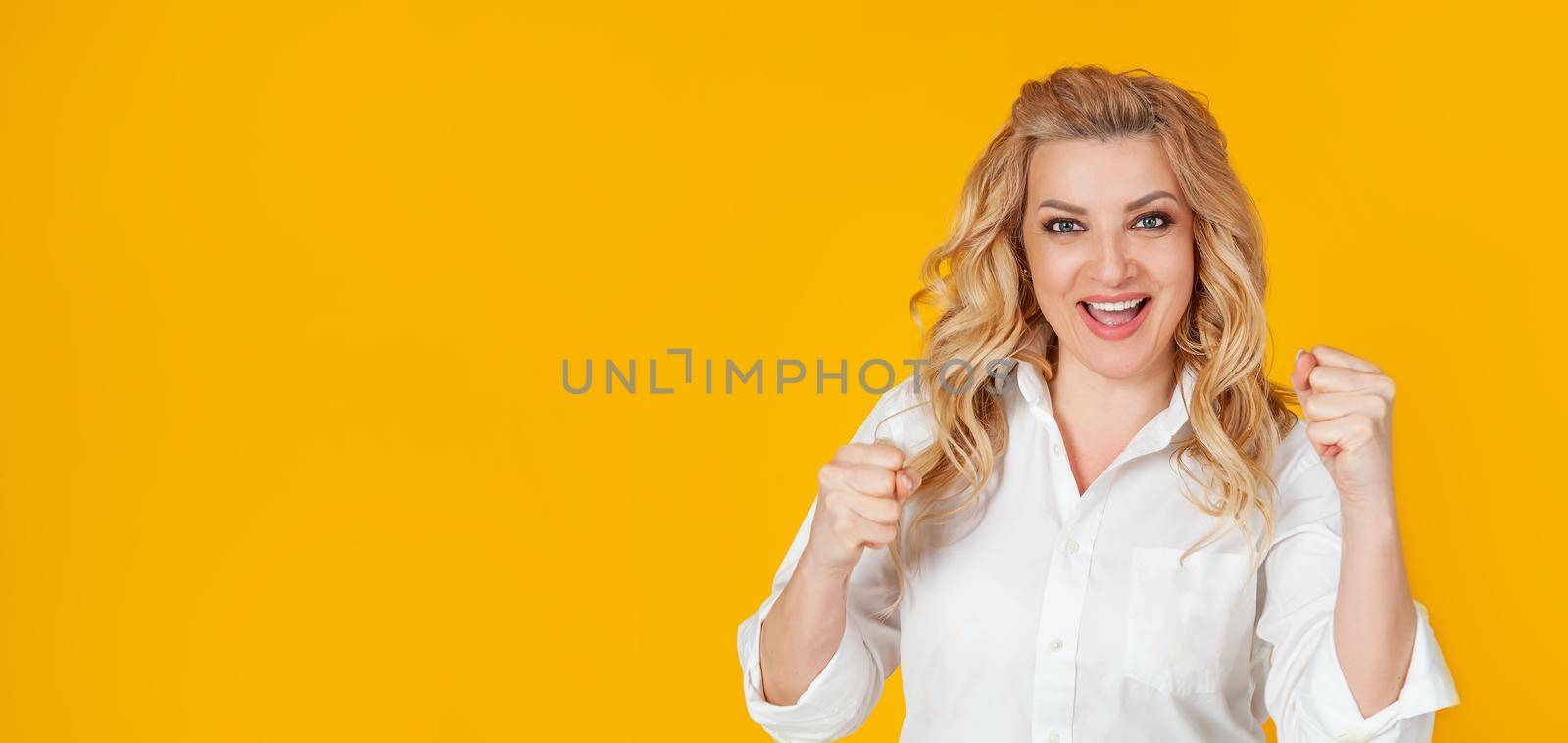 Cheerful, happy woman raising her hands with her fist, cheering for the team, winning a huge bet, playing in the casino in delight, cheering friends, watching football, yellow background