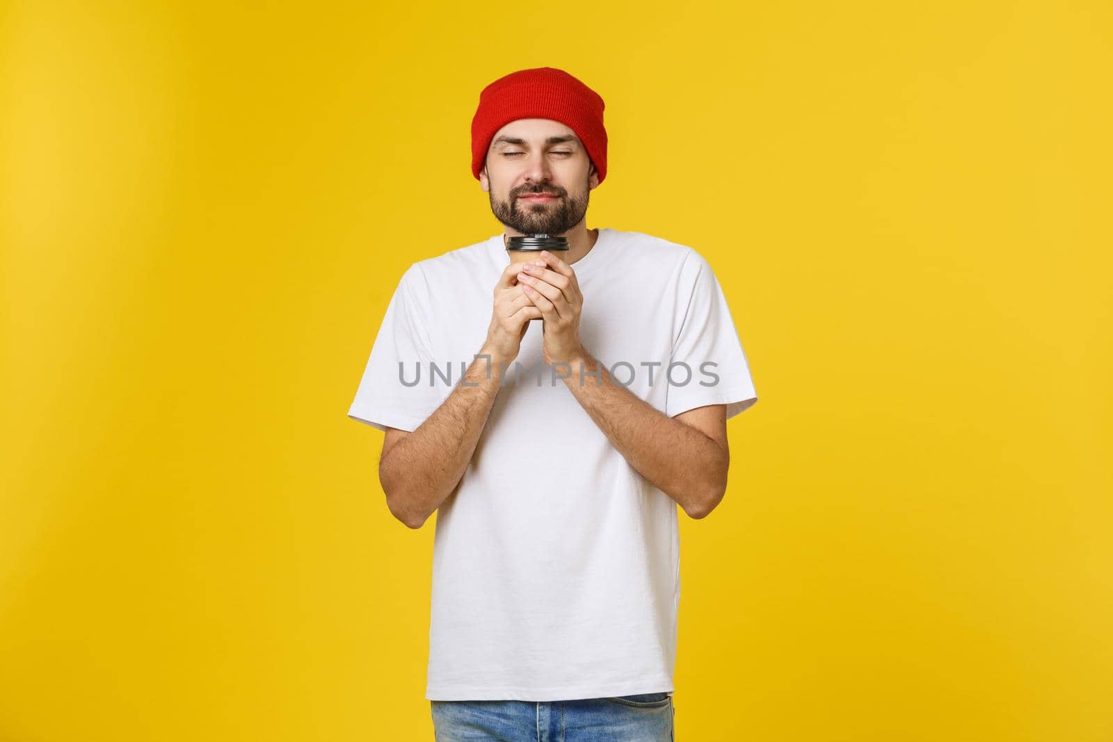 Man on isolated vibrant yellow color taking a coffee in takeaway paper cup and smiling because he will start the day well