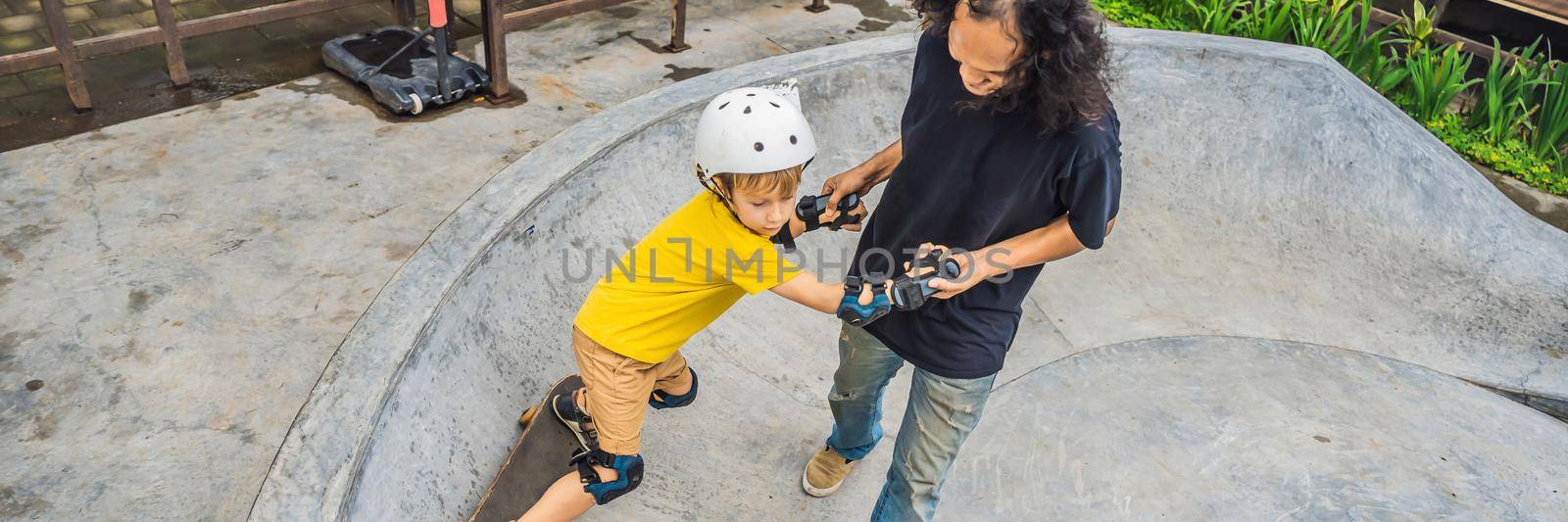 Athletic boy learns to skateboard with asian trainer in a skate park. Children education, sports. Race diversity BANNER, LONG FORMAT by galitskaya