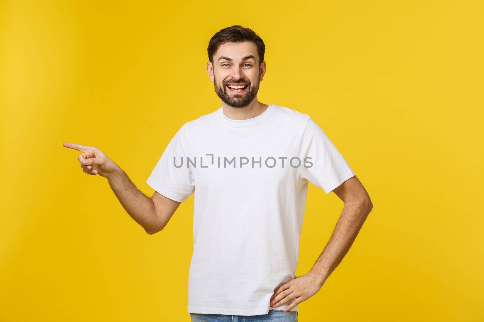 Man pointing showing copy space isolated on yellow background. Casual handsome Caucasian young man. by Benzoix