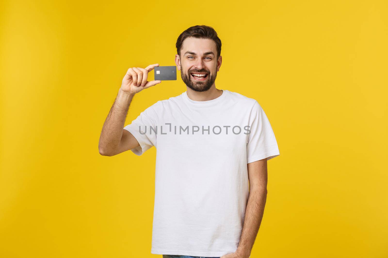 Happy smiling young man showing credit card isolated on yellow background.