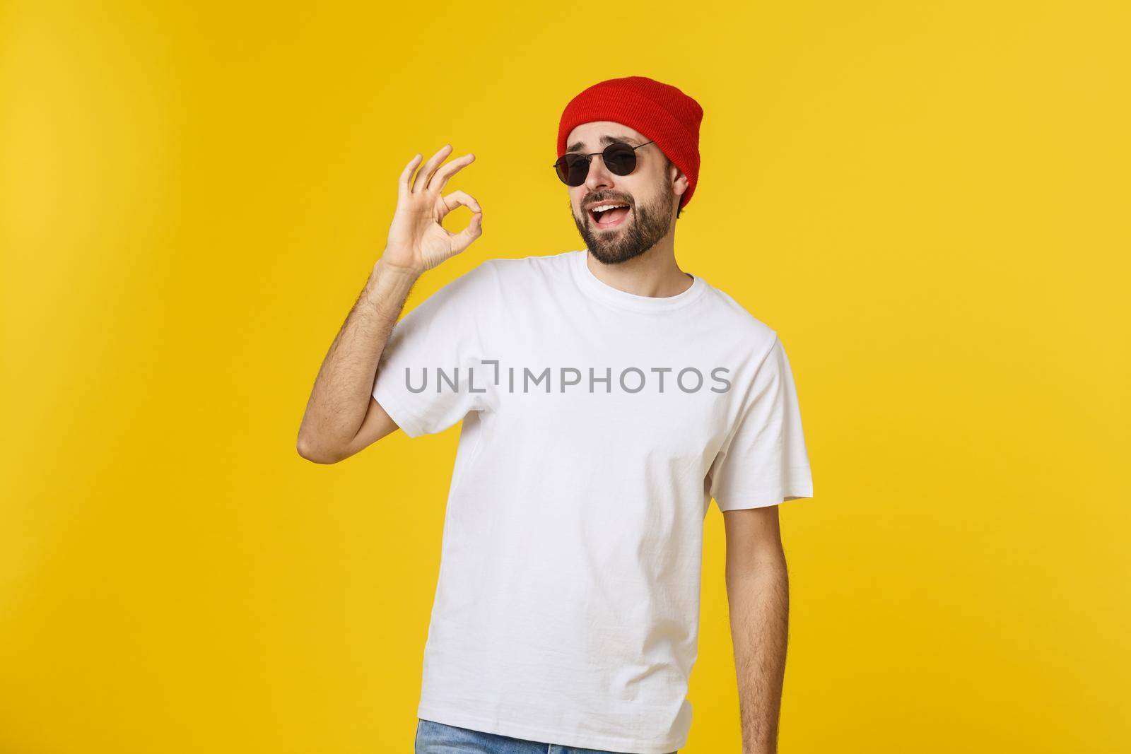 Satisfied young man showing okay sign isolated on yellow background. by Benzoix