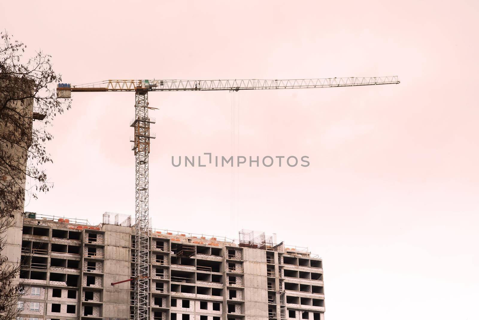 Construction crane is working on the construction of a multi-storey building, the view from the bottom of the crane on the construction crane and the building under construction against the sky.
