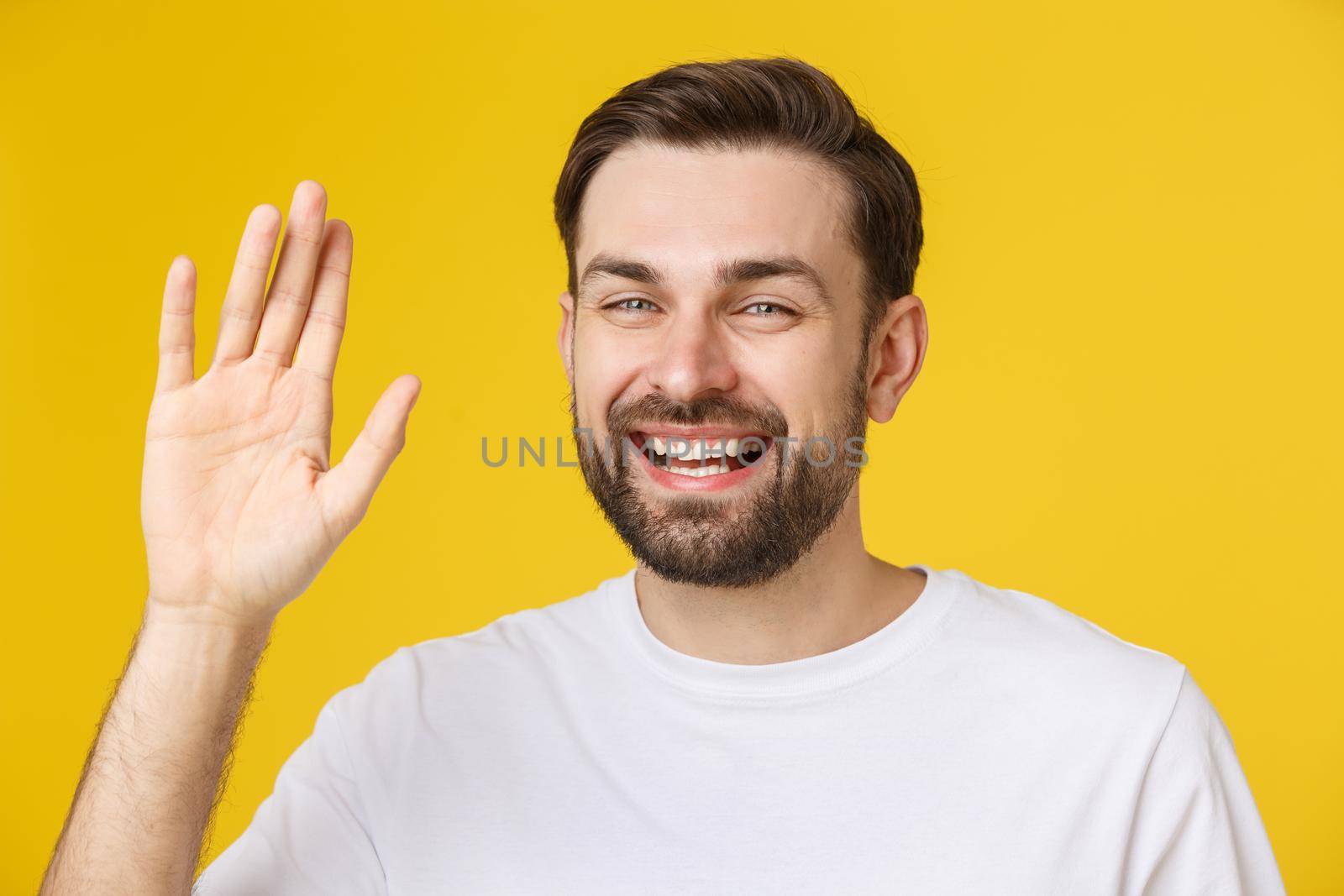 Hi, Hello. Portrait of happy friendly brown-haired man with small beard in white shirt waving hand to camera, welcoming with toothy smile. by Benzoix