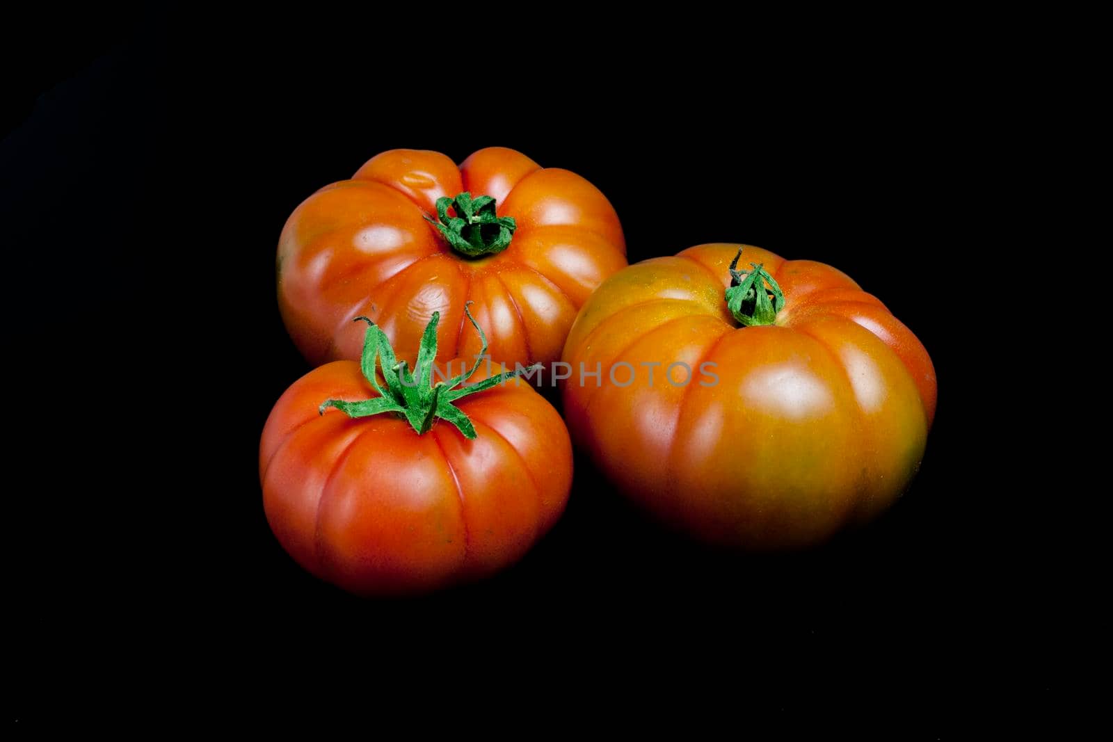 Three whole ripe tomatoes on a black background