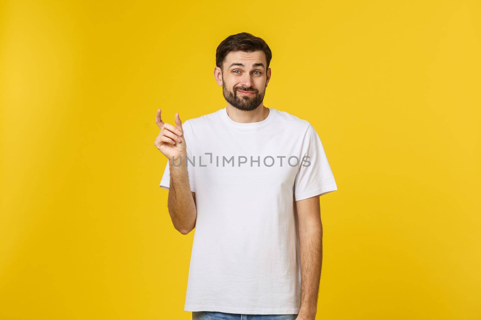 Caucasian man show small size by fingers demonstrate tiny measure, tell about little decreased prices. Studio shot yellow wall.