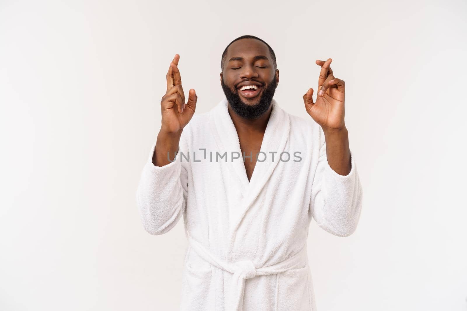 Headshot of African American man crossing fingers wishing and praying for miracle, hoping for the best, isolated against white copy space wall. Positive human emotions, expressions and feelings