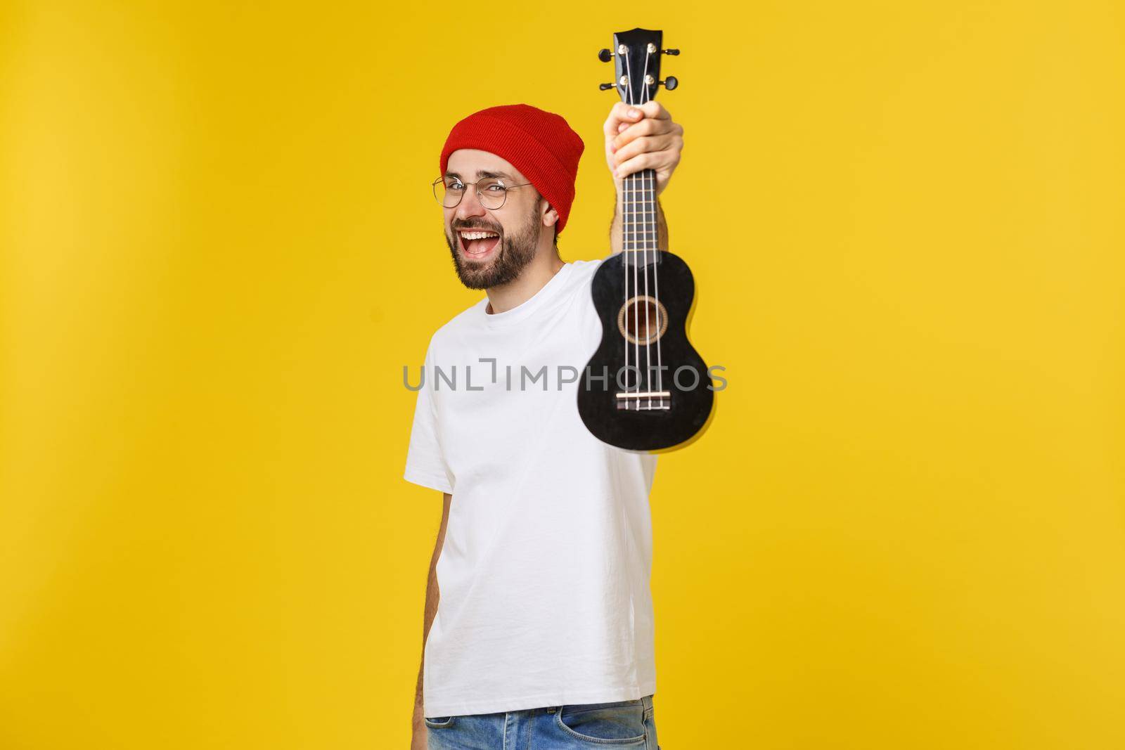 close-up of funny young man playing a guitar. isolated on yellow gold background.