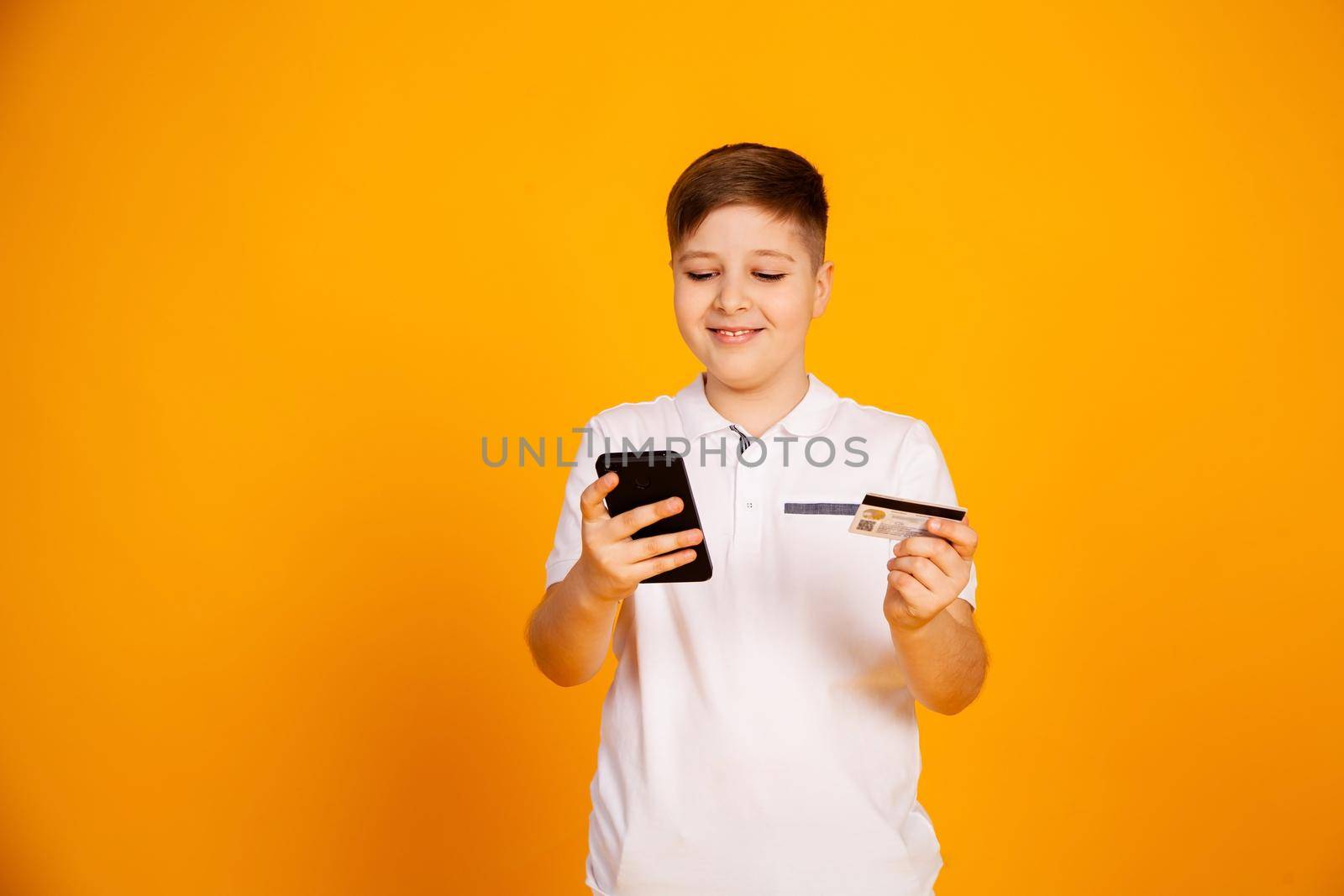 The boy holds a credit card and the smartphone makes purchases. Happy young man uses a smartphone and a bank card to shop online. Handsome smiling guy holds a bank card and mobile phone