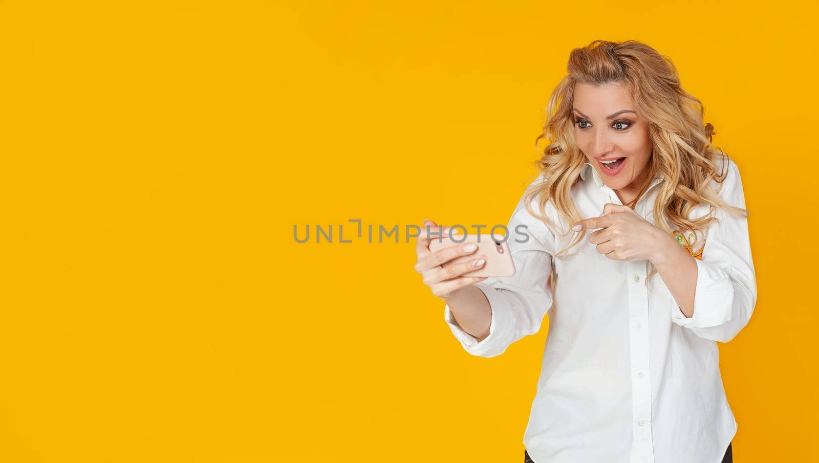 Technology, online lifestyle concept. Caucasian blond woman rejoicing in victory in the game, showing her finger on a smartphone, saying yes, cheers, pleased with a smile on a mobile phone,