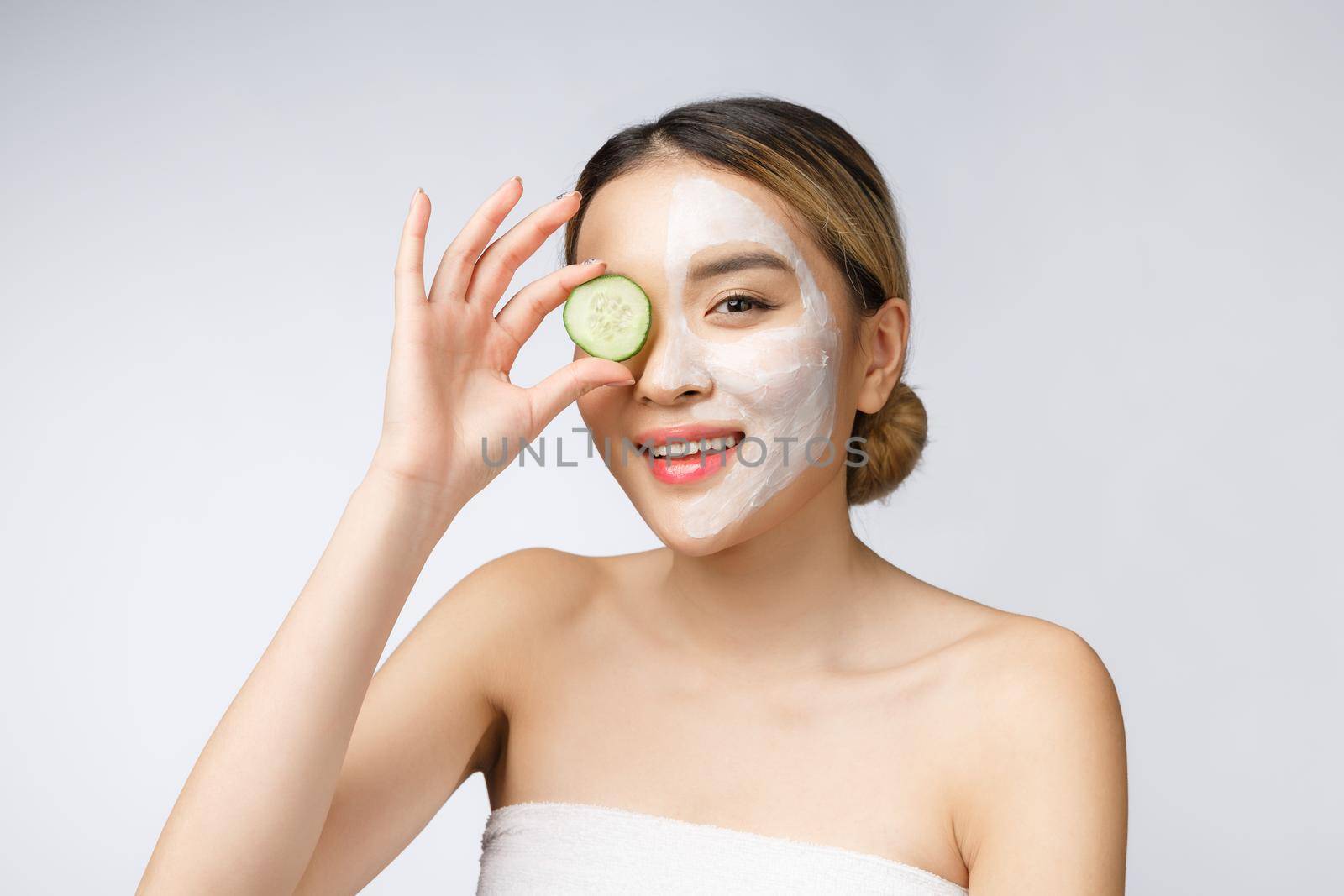 Asian young beautiful smiling woman with flawless complexion holding cucumber slices over eye