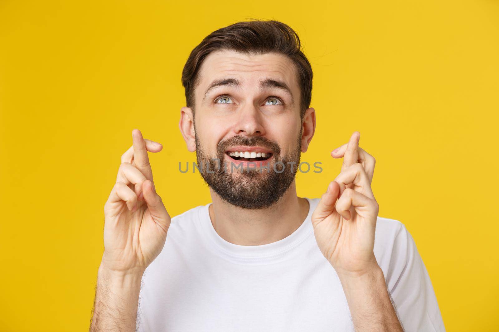 Young man making a wish isolated on yellow background.