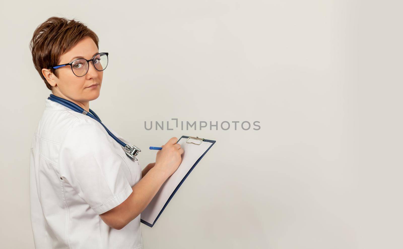 Female doctor writes with a pen a document on a tablet, writes a medical history. The concept of healthcare, medicine and pharmacy.