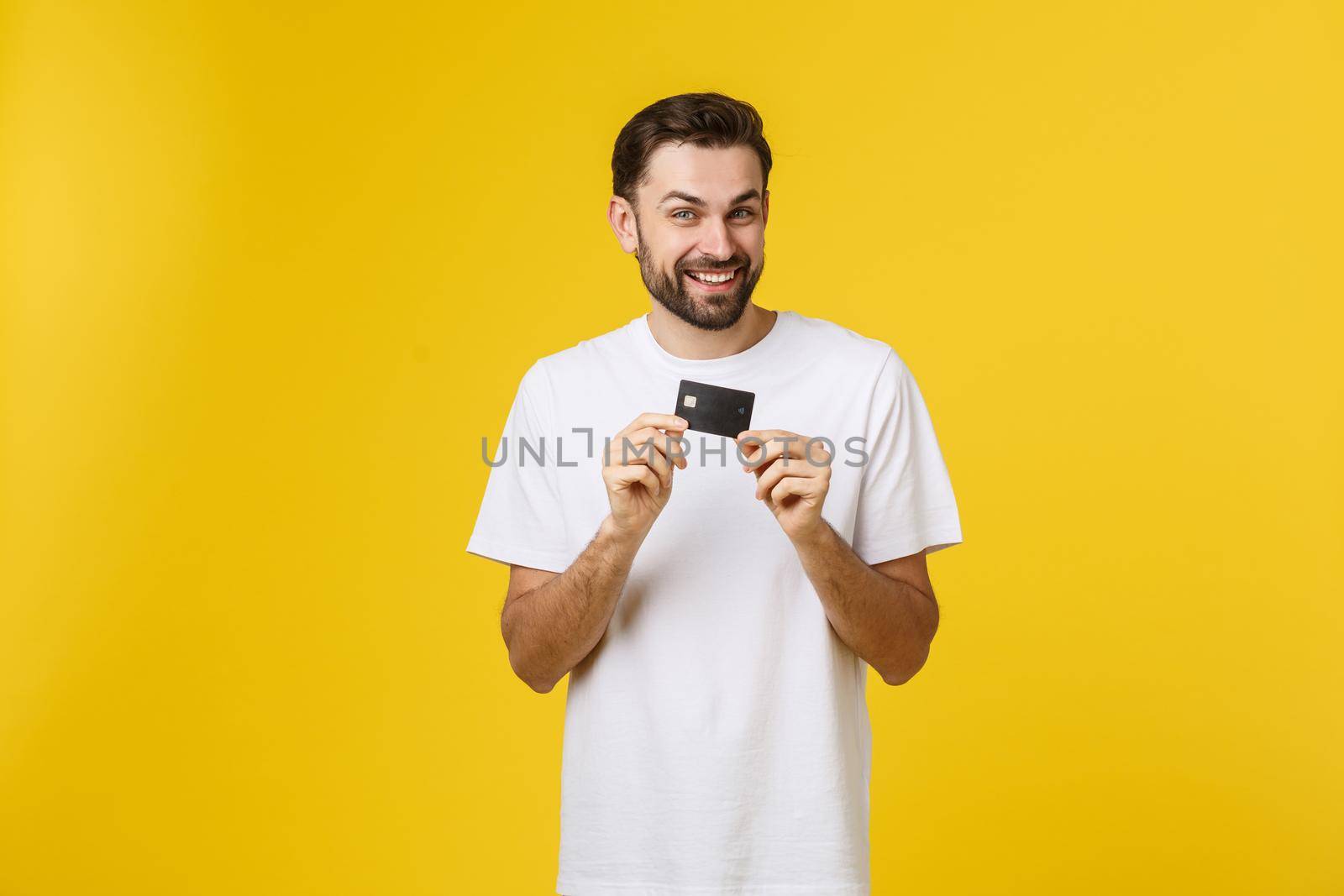 Happy smiling young man showing credit card isolated on yellow background by Benzoix