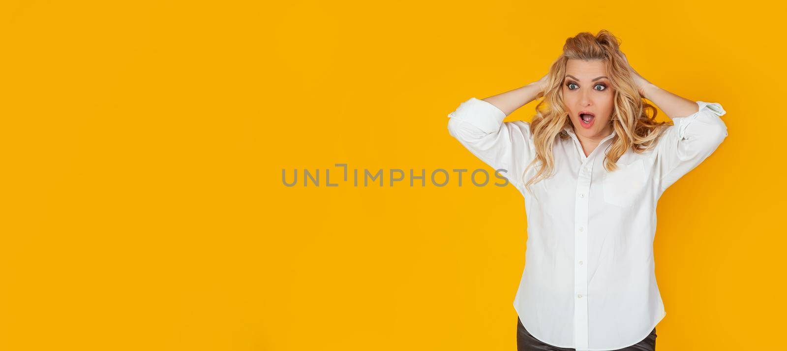Portrait of a woman in a panic with her hands clutching her head, excited and looking panicky down, hands clutching her head, breaking an expensive thing, alarmed indecisive, on a yellow background